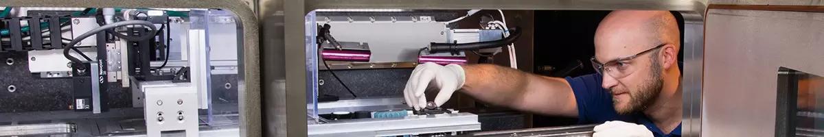 A man peers into a piece of manufacturing lab equipment